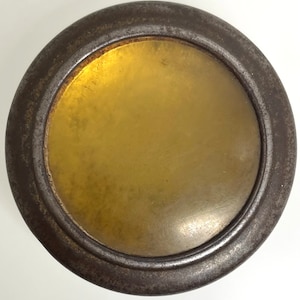Könnte beinhalten: Ein runder, metallener Deckel mit einer goldfarbenen Mitte. Der Deckel hat einen leicht erhöhten Rand um die Mitte.
