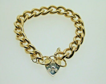 Op de afbeelding: Een gouden kettingarmband met een hartvormige slot sluiting. De ketting is dik en heeft een platte schakels ontwerp.