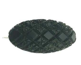May include: A black carved glass oval brooch with a geometric pattern.