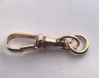 May include: A gold-colored swivel clasp with a spring-loaded hook on one end and two connected rings on the other. The clasp is designed to rotate, allowing for flexible attachment. The metal has a polished finish.