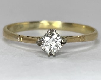 May include: A gold band engagement ring with a single round diamond set in a white metal setting.