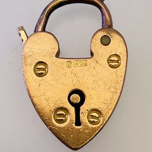 Könnte beinhalten: Ein goldener herzförmiger Schlossanhänger mit einem Schlüsselloch und einer 9375-Stempelung. Der Anhänger hat einen abgenutzten, antiken Look.