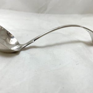 以下が含まれることがあります： 曲がった柄と丸いボウルが付いた銀色のレードル。レードルは光沢のある反射性の金属でできており、スープやソースの提供に使用されます。ハンドルは優雅にカーブし、装飾的な形で終わっています。