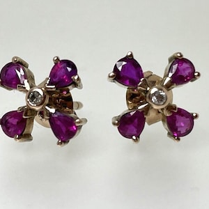 Op de afbeelding: Een paar gouden oorbellen met een bloemmotief. Elke oorbel heeft vijf robijnstenen in een peervorm en een enkele diamant in het midden.