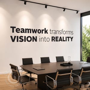 Könnte beinhalten: Ein Wandaufkleber mit dem schwarzen Text Teamwork transforms VISION into REALITY auf einer weißen Bürowand über einem dunklen Konferenztisch mit schwarzen Stühlen und einem an der Decke montierten Schienenbeleuchtungssystem.