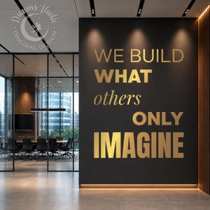 以下が含まれることがあります： WE BUILD WHAT others ONLY IMAGINEという金色の金属文字が施された大きなマットブラックの壁。この壁は、ガラスのパーティション、会議用テーブル、椅子が見えるモダンなオフィススペースに設置されています。