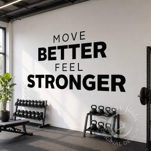 May include: A gym interior with a white wall featuring the motivational phrase "MOVE BETTER FEEL STRONGER" in black. Dumbbells and kettlebells are stored on racks. A weightlifting station is visible. A bench and a plant are also present.