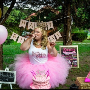 Puede incluir: Una mujer con una falda de tul rosa y una camiseta blanca con el texto "The Birthday Girl" sostiene una copa de vino y una botella de champ&aacute;n. Est&aacute; de pie frente a un pastel de cumplea&ntilde;os rosa y dorado con el n&uacute;mero 35. Detr&aacute;s de ella hay un cartel que dice "Karen" con una lista de cosas que le gustan.