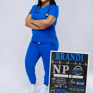 K&ouml;nnte beinhalten: Eine Frau in blauen OP-Kleidung steht vor einem schwarzen Schild aus Schiefer, auf dem "BRANDI NP Klasse von 2022" steht, mit einem Stethoskop um den Hals. Das Schild enth&auml;lt auch den Text "University of Memphis", "Zu viele Erdbeer-Frappuccinos zum Z&auml;hlen", "Unmengen an B&uuml;chern", "Endlose Stunden des Lernens", "&Uuml;ber 750 Praktikumsstunden", "Ein Abschluss n&auml;her", und "Was Gott verordnet hat, kann nicht gestoppt werden."