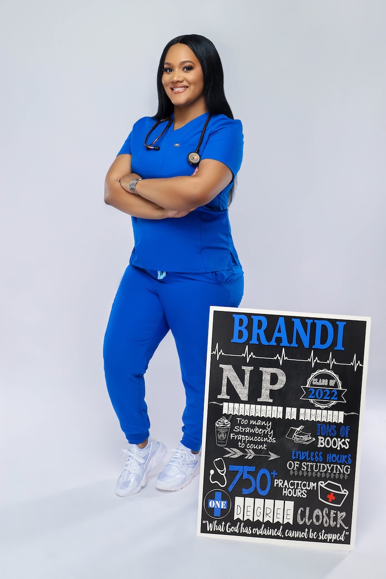 K&ouml;nnte beinhalten: Eine Frau in blauen OP-Kleidung steht vor einem schwarzen Schild aus Schiefer, auf dem "BRANDI NP Klasse von 2022" steht, mit einem Stethoskop um den Hals. Das Schild enth&auml;lt auch den Text "University of Memphis", "Zu viele Erdbeer-Frappuccinos zum Z&auml;hlen", "Unmengen an B&uuml;chern", "Endlose Stunden des Lernens", "&Uuml;ber 750 Praktikumsstunden", "Ein Abschluss n&auml;her", und "Was Gott verordnet hat, kann nicht gestoppt werden."