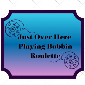 May include: A decorative sign with a blue and purple gradient background and the text "Just Over Here Playing Bobbin Roulette." The sign has a dark purple border and features illustrations of sewing machine bobbins. A floral logo with scissors is at the bottom.
