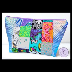 May include: A zippered pouch featuring a patchwork design of various colorful fabrics, including patterns of zebras, pandas, teacups, and coral. The side panels are made of a textured, iridescent blue material, and a purple zipper runs along the top.