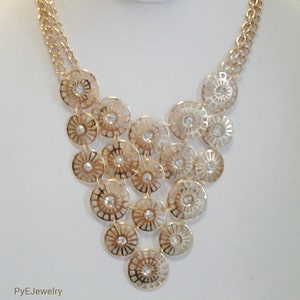 May include: A gold necklace with a layered design of circular pendants. Each pendant is made of a delicate, openwork metal with a small rhinestone in the center. The necklace is on a white mannequin.