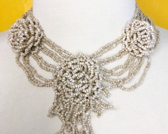 Collar babero de varias hebras con rosas y cuentas de semillas de color beige.