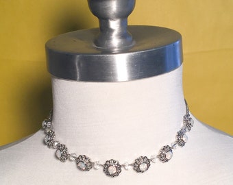 Collar babero con pequeñas flores de plata y cuentas de cristal blanco.