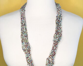 Collar largo de cuentas de semillas de color azul, verde, marrón y beige.