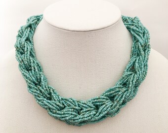 Collar con babero de cuentas de semillas trenzadas de múltiples hebras de color verde azulado.