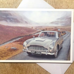 May include: A silver-grey classic car drives on a winding road through a misty mountain landscape. The car's license plate reads "BMT 216A".