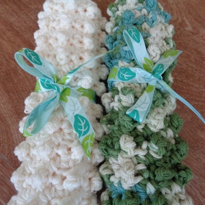May include: Two crocheted scrubbies, one white and one green and blue, tied together with a blue ribbon with green leaf accents.
