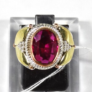 May include: A ring with a large, oval-shaped, dark pink gemstone set in a gold and silver band. The band is decorated with a beaded design.