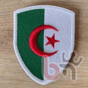 May include: A white and green embroidered patch with a red crescent moon and star in the centre. The patch is shaped like a shield.