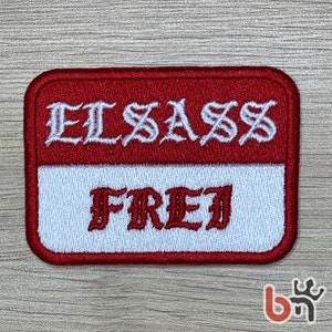 Op de afbeelding: Rode en witte geborduurde patch met de tekst "ELSASS FREI" in een gestileerd lettertype.