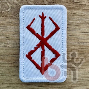 Può includere: Una toppa rettangolare con sfondo bianco e un simbolo rosso. Il simbolo è un design astratto stilizzato con angoli acuti e una linea verticale centrale. La toppa ha un bordo bianco con bordi cuciti.