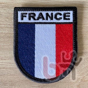 Puede incluir: Un parche bordado en negro y blanco con la palabra "FRANCE" en letras blancas y los colores de la bandera francesa: azul, blanco y rojo.