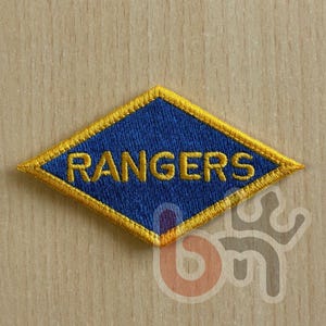 Könnte beinhalten: Gestickter Aufnäher mit dem Wort „RANGERS“ in goldfarbenen Buchstaben auf einem blauen Rautenmuster, goldfarben umrandet. Für Uniformen oder Kleidung.