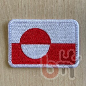 Könnte beinhalten: Gestickter Aufnäher mit der Flagge Grönlands. Der rechteckige Aufnäher hat einen weißen Hintergrund mit einem roten Kreis und einem roten Streifen am unteren Rand. Der Aufnäher ist mit weißen Nähten eingefasst.