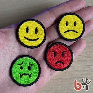 May include: Four embroidered iron-on patches with different facial expressions. The patches are yellow, red, green, and yellow. The expressions are smiling, frowning, sad, and angry.
