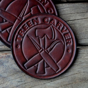 May include: Four brown leather coasters with a tooled design of crossed tools and the text "Tree Carver".