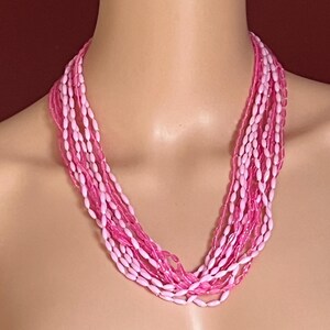 Puede incluir: Un collar de m&uacute;ltiples hilos con cuentas ovaladas rosas y blancas. El collar se muestra en un maniqu&iacute;, destacando el dise&ntilde;o en capas y las variaciones de color. Las cuentas est&aacute;n ensartadas, creando un efecto en cascada.