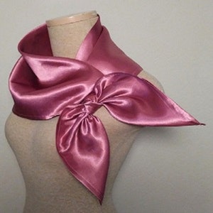 May include: A pink satin scarf tied in a bow. The scarf is draped around a mannequin's neck.