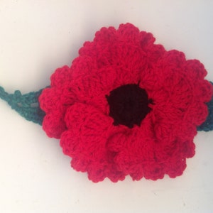 May include: A red crocheted poppy flower with a black center and a green crocheted stem.