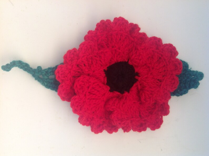 May include: A red crocheted poppy flower with a black center and a green crocheted stem.