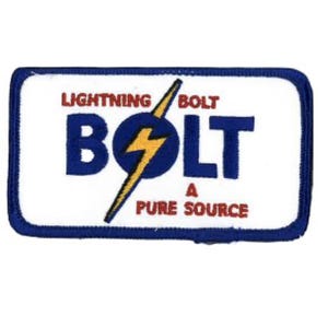 May include: A rectangular embroidered patch with a white background and a blue border. It features the blue text BOLT, a yellow lightning bolt graphic, and the red text LIGHTNING BOLT A PURE SOURCE. The design is centred on the white fabric surface.