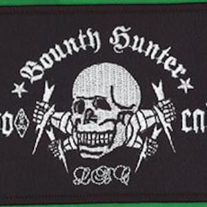Pode incluir: Patch retangular preto com design bordado branco. O design apresenta uma caveira, raios e as palavras "Bounty Hunter" e "80 cal". Duas estrelas ladeiam as palavras. O patch tem uma borda verde.