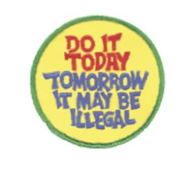 Op de afbeelding: Een ronde geborduurde patch met een gele achtergrond en een groene gestikte rand. De tekst luidt DO IT TODAY in het rood, gevolgd door TOMORROW IT MAY BE ILLEGAL in het blauw, alles in een vet, enigszins onregelmatig, handgetekend lettertype.