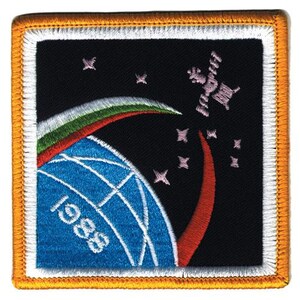 May include: A square embroidered patch featuring a black background with a blue globe showing the year 1986. A space station orbits above with pink stars, a green and red curved arc, and a white border finished with an orange stitched edge.