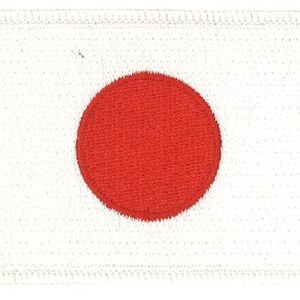 May include: A rectangular embroidered patch featuring a white background with a solid red circle centered in the middle. The patch has a stitched border around the entire perimeter, creating a clean edge for attachment to fabric or other surfaces.