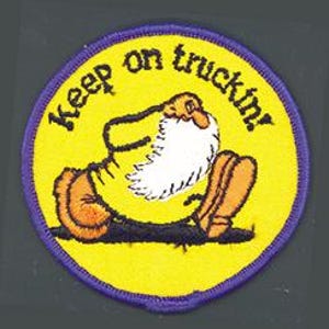 May include: A circular embroidered patch with a yellow background and a purple border. It features a cartoon character with a large white beard and brown boots, walking across a black line. The text "Keep on truckin'" is printed in black.