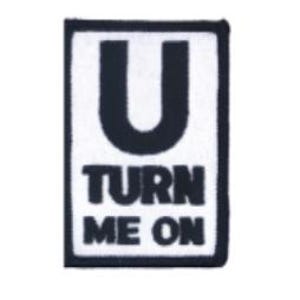 May include: A rectangular embroidered patch featuring a white background with a thick black border. The patch displays the black text U TURN ME ON, with the letter U positioned above the words TURN and ME ON in a stacked, bold font style.