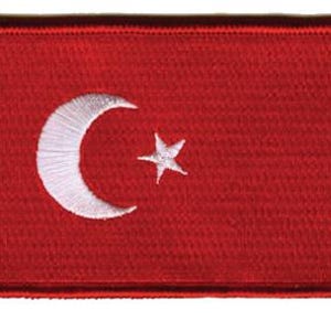 May include: A rectangular embroidered patch featuring a solid red background with a white crescent moon and a five-pointed star centered on the fabric. The edges of the patch are finished with a thick, stitched border in a matching red thread.