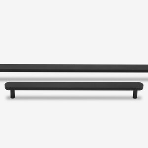 May include: Two black metal cabinet pulls with rounded edges. The top pull is longer than the bottom pull.