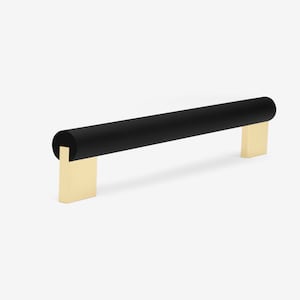 May include: Black cylindrical cabinet pull with gold metal end caps. The pull is approximately 10 inches long.