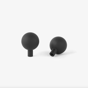 May include: Two matte black spherical cabinet knobs with short cylindrical stems. One knob is upright, the other is angled. The knobs are set against a plain white background, highlighting their simple, modern design.