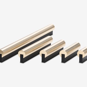 May include: Five different sizes of gold-toned cabinet hardware with black bases. The hardware is in the shape of a rounded rectangle.