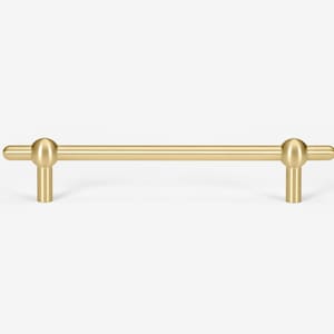 May include: A gold-toned cabinet pull with rounded ends. The pull is a simple, straight bar with a slight curve at each end.