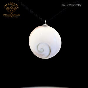 Puede incluir: Un colgante circular de concha de ojo de Shiva con un patrón de espiral natural, suspendido de un cordón negro fino. El colgante incluye una anilla de metal plateado en la parte superior. El texto MANGAL BM GEMS JEWELRY y BMGemsJewelry aparece.